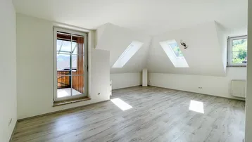Helles Zimmer im Dachgeschoss mit Laminatboden, Dachschrägen und Zugang zu einem Balkon.
