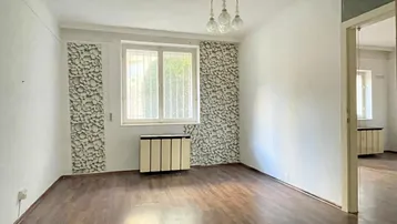 Helles Wohnzimmer mit dunklem Laminatboden, einem Heizkörper und Blick ins Grüne durch das Fenster.
