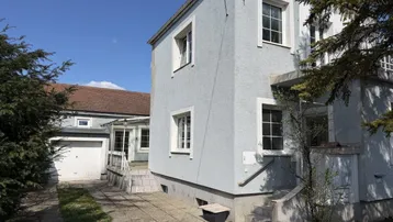 Graues Haus mit weißem Garagentor und gepflasterter Auffahrt unter blauem Himmel.
