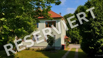 Charmantes Wohnhaus mit hellgrüner Fassade und rotem Ziegeldach, umgeben von einem gepflegten Garten mit altem Baumbestand.