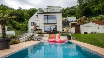 Moderne Villa mit weißer Fassade, großen Fenstern und einem einladenden Poolbereich im Vordergrund.
