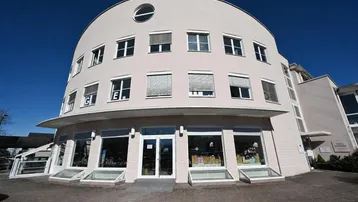 Gebäude mit moderner, geschwungener Fassade und großen Schaufenstern im Erdgeschoss.