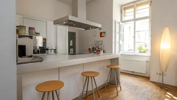 Funktionale Küche mit Frühstücksbar und Hockern, hell durch großes Fenster und Stehlampe.
