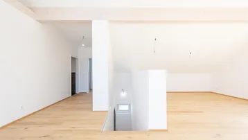 Heller, offener Raum mit Holzbalken und Parkettboden, der zu einem Flur und einer Treppe führt.