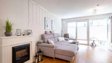 Helles Wohnzimmer mit gemütlichem Sofa, Kamin und Zugang zur Terrasse.