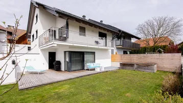 Modernes Haus mit großer Holzterrasse, Garten und Balkonen, ideal für entspannte Stunden im Freien.