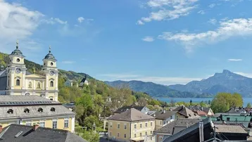 Malerischer Blick über eine Stadt mit historischer Kirche, See und majestätischen Bergen im Hintergrund.