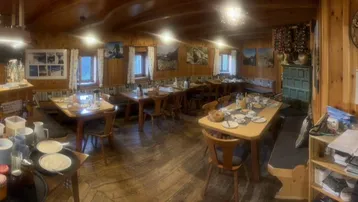 Geräumiger Speisesaal einer Berghütte mit Holzwänden, Holzböden und mehreren Tischen für Gäste.