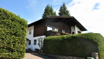 Traditionelles Haus mit Holzbalkonen und gepflegter Hecke unter blauem Himmel.