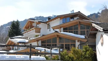 Charmantes Chalet mit traditioneller Holzarchitektur, großen Fenstern und schneebedeckten Dächern vor Bergkulisse.