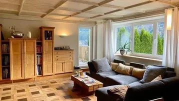 Helles Wohnzimmer mit Holzkassettendecke, Parkettboden und Blick ins Grüne sowie Balkonzugang.