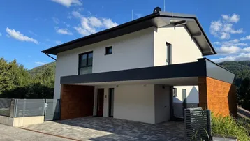 Moderne Hausfassade mit Carport und gepflasterter Einfahrt unter blauem Himmel.