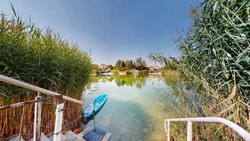 Treppe führt direkt in den See, umgeben von Schilf, mit einem Kajak im Wasser und Häusern am gegenüberliegenden Ufer.