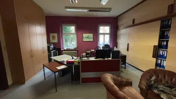 Geräumiges Büro mit Holzschränken, roter Akzentwand und zwei Fenstern, die Tageslicht hereinlassen.