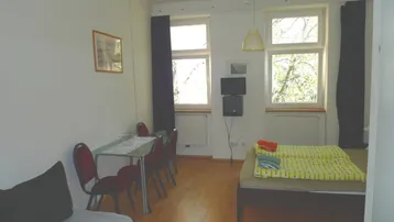 Helles Zimmer mit Bett, Esstisch und Parkettboden, ideal für Einzelpersonen oder Paare.