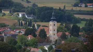 Panoramablick auf ein malerisches Dorf mit einer prominenten Kirche und grüner Landschaft.