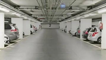 Geräumige Tiefgarage mit zahlreichen Stellplätzen, Betonpfeilern und sichtbaren Installationen an der Decke.