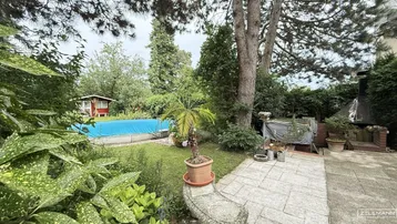 Großer Gartenbereich mit überdachtem Pool, Gartenhaus und gepflasterter Terrasse, umgeben von viel Grün.