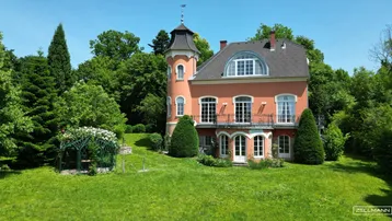 Historische Villa mit Turm und weitläufigem, gepflegtem Garten unter blauem Himmel.