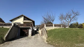 Einfamilienhaus mit Zufahrt zur Tiefgarage und gepflastertem Vorplatz unter blauem Himmel.