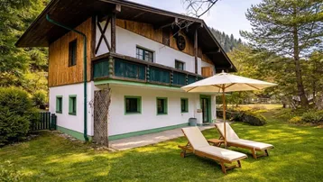 Traditionelles Chalet mit Balkon, großer Rasenfläche und Terrasse mit Liegestühlen, umgeben von Bergen und Natur.