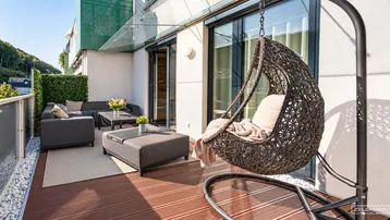 Geräumiger Balkon mit bequemen Outdoor-Möbeln, Hängesessel und Blick ins Grüne.