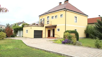 Gelbes Einfamilienhaus mit rotem Ziegeldach, Garage, gepflasterter Auffahrt und gepflegtem Garten.
