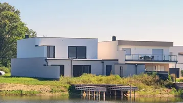 Moderne Häuser am Wasser mit Steg und Blick auf die umliegende Natur und den See.