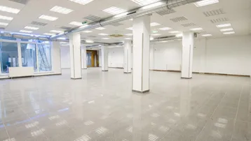 Großer, offener Gewerberaum mit Säulen, Fliesenboden und sichtbaren Lüftungsrohren an der Decke.