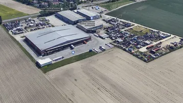 Luftaufnahme eines Industriegebiets mit großen Hallen, Parkplätzen und umliegenden Feldern.