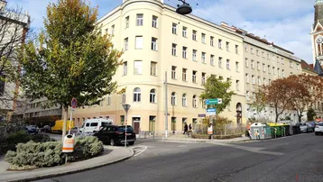 Gebäude an einer Straßenecke mit klassischer Architektur, Bäumen und parkenden Autos im Herbst.