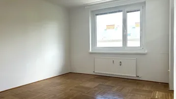 Helles Zimmer mit Fischgrätparkettboden und großem Fenster, ideal als Wohn- oder Schlafzimmer.