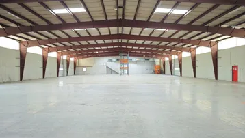 Große, leere Lagerhalle mit hohen Decken, sichtbaren Stahlträgern und Betonboden, ideal für industrielle Nutzung.