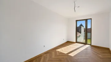 Helles Zimmer mit Fischgrätparkett und großem Fenster, das viel Sonnenlicht hereinlässt.