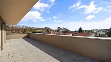 Geräumige Dachterrasse mit Fliesenboden und weitem Blick über die Landschaft unter blauem Himmel.