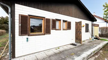 Seitenansicht eines Hauses mit weißer Holzverkleidung und braunen Fensterläden.