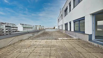 Große Dachterrasse mit Betonplatten und Blick auf umliegende Gebäude unter blauem Himmel.