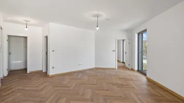 Heller, leerer Wohnbereich mit modernem Fischgrätparkett und Zugang zu weiteren Räumen.