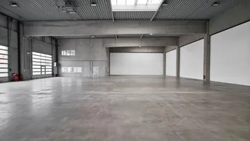 Geräumige, leere Lagerhalle mit hohen Decken, Betonboden und großen Rolltoren, ideal für industrielle Nutzung.