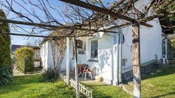 Kleiner Gartenbereich mit Pergola und Sitzgelegenheit neben dem Haus, ideal für entspannte Stunden im Freien.