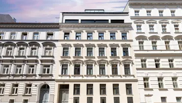 Historische Fassade eines Mehrfamilienhauses mit klassischer Architektur und modernen Dachaufbauten.