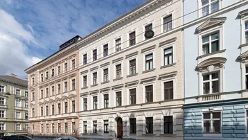 Historisches Gebäude mit traditioneller Fassade und parkenden Autos auf der Straße unter blauem Himmel.