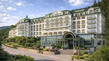 Elegantes Hotelgebäude mit vielen Balkonen und grünen Dächern, umgeben von üppiger Natur.