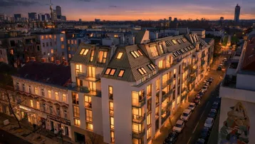 Abendliche Luftaufnahme eines modernen Wohngebäudes mit beleuchteten Fenstern und Stadtblick.