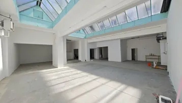 Großer, heller Gewerberaum mit beeindruckendem Glasdach, Betonboden und hohen Decken.
