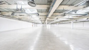 Großer, leerer Gewerberaum mit poliertem Betonboden und sichtbaren Lüftungsrohren an der Decke.