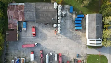 Luftaufnahme eines weitläufigen Gewerbegeländes mit mehreren Hallen, Lagerflächen und Fahrzeugen.