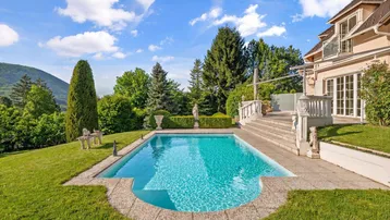 Außenbereich mit großem Pool, Steinterrasse und Blick auf die umliegende grüne Landschaft.