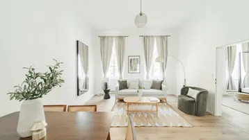 Gemütliches Wohnzimmer mit Holzboden, beigen Vorhängen und Blick auf die Straße.