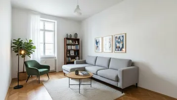 Helles Wohnzimmer mit modernem Sofa, Sessel und Bücherregal, ausgestattet mit Fischgrätparkett.